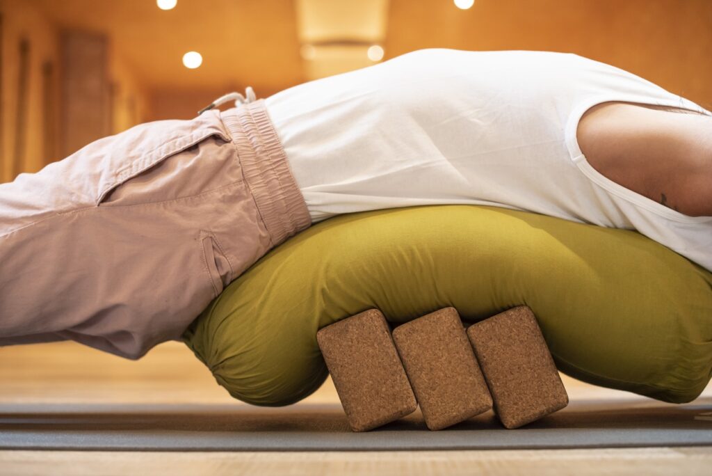 posture de yoga restauratif avec bolster et briques, utilisées en formation pour accompagner le relâchement et la détente