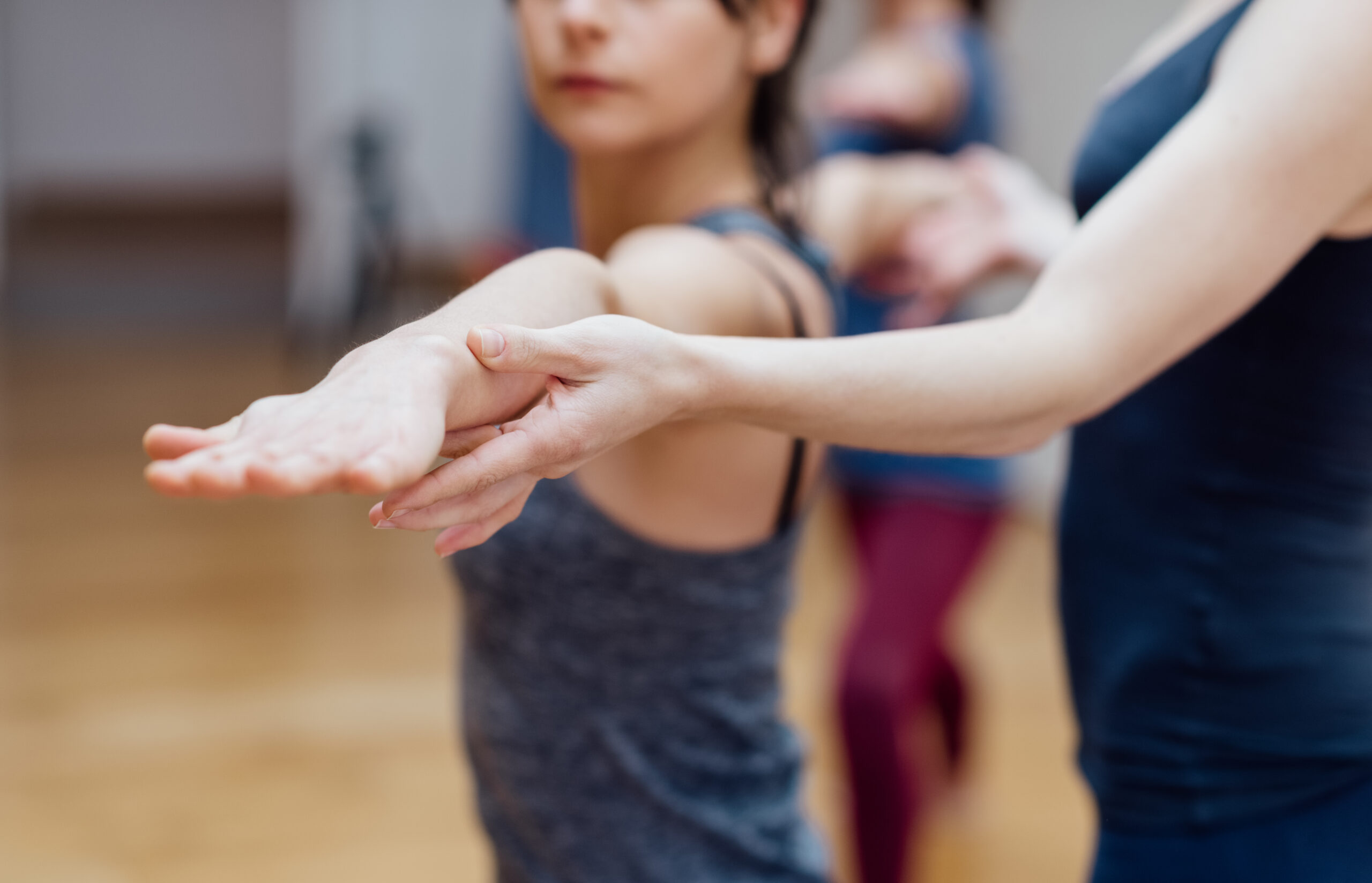 Ajustement yoga par le toucher sur le bras d'une pratiquante, démontrant un accompagnement pédagogique précis et respectueux en cours de yoga